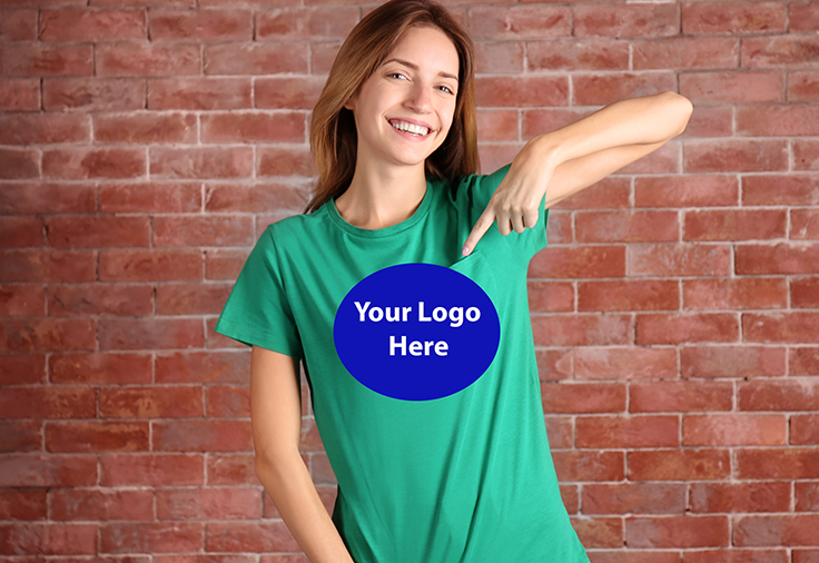 A joyous woman pointing at a blue circle printed on her green t-shirt, which reads 'Your logo here'.