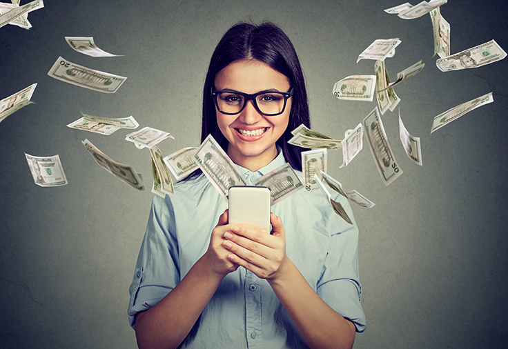 A smiling woman holding a mobile device with $20 bills emerging from it into the air.
